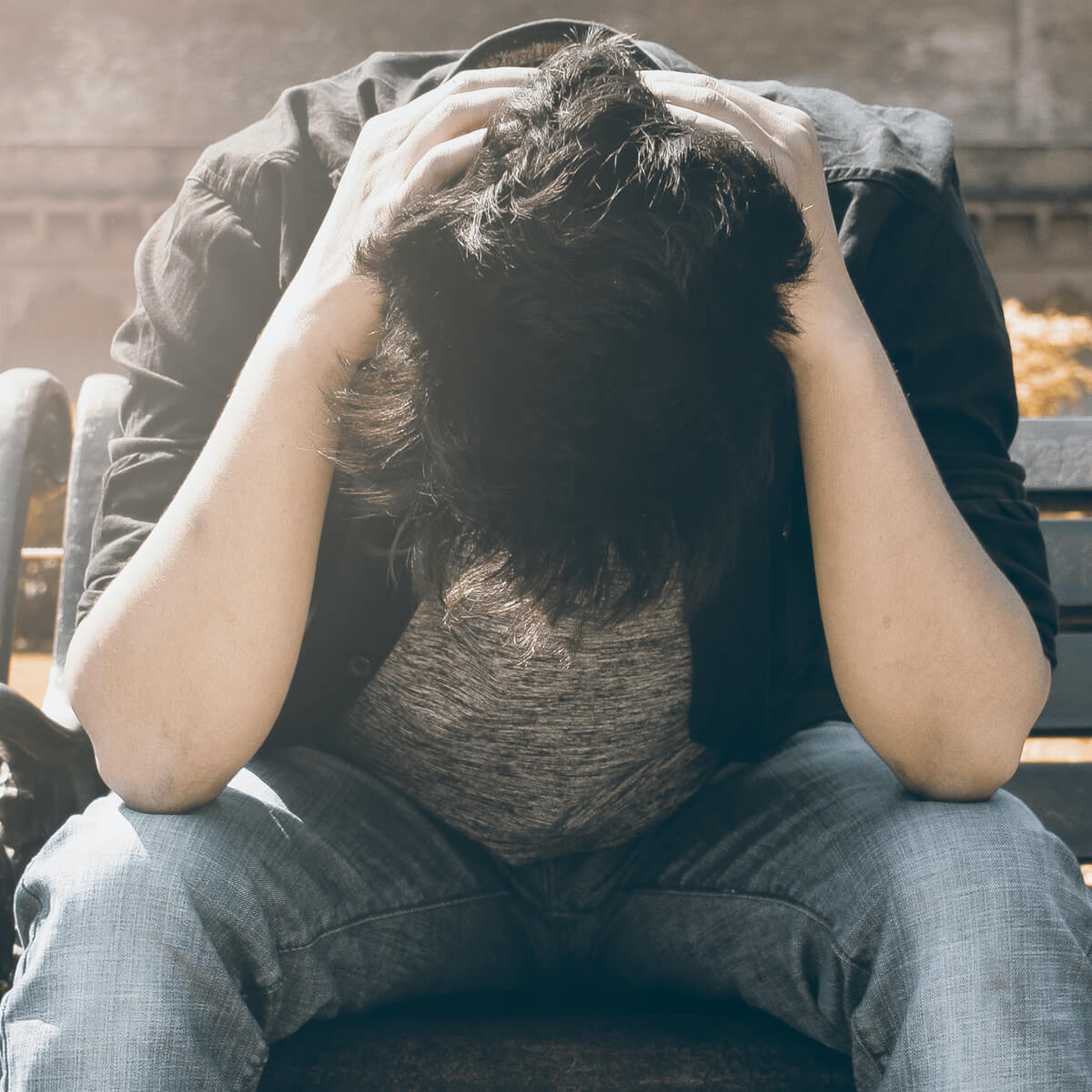 You teenage boy holding head looking at floor, depressed